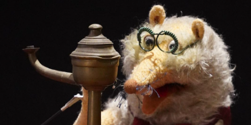 Ein Tier-Handpuppe mit einer Brille, die mit einem altertümlichen Telefon telefoniert.