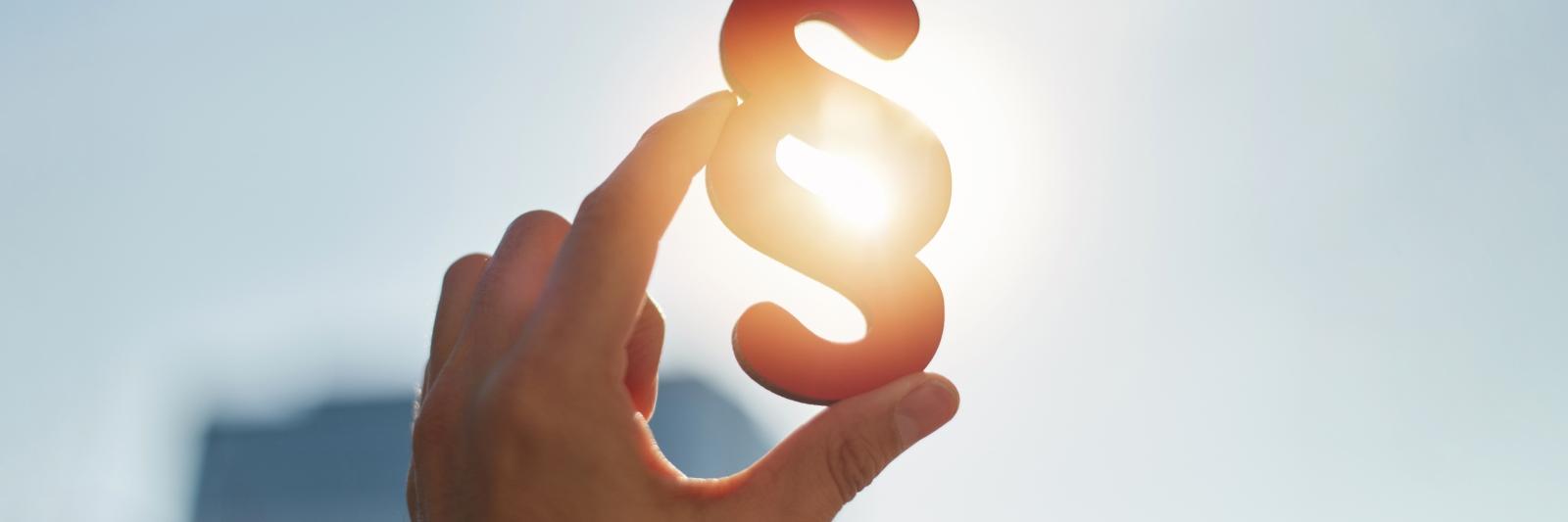 Hand holds paragraph symbol in the sun in the sky