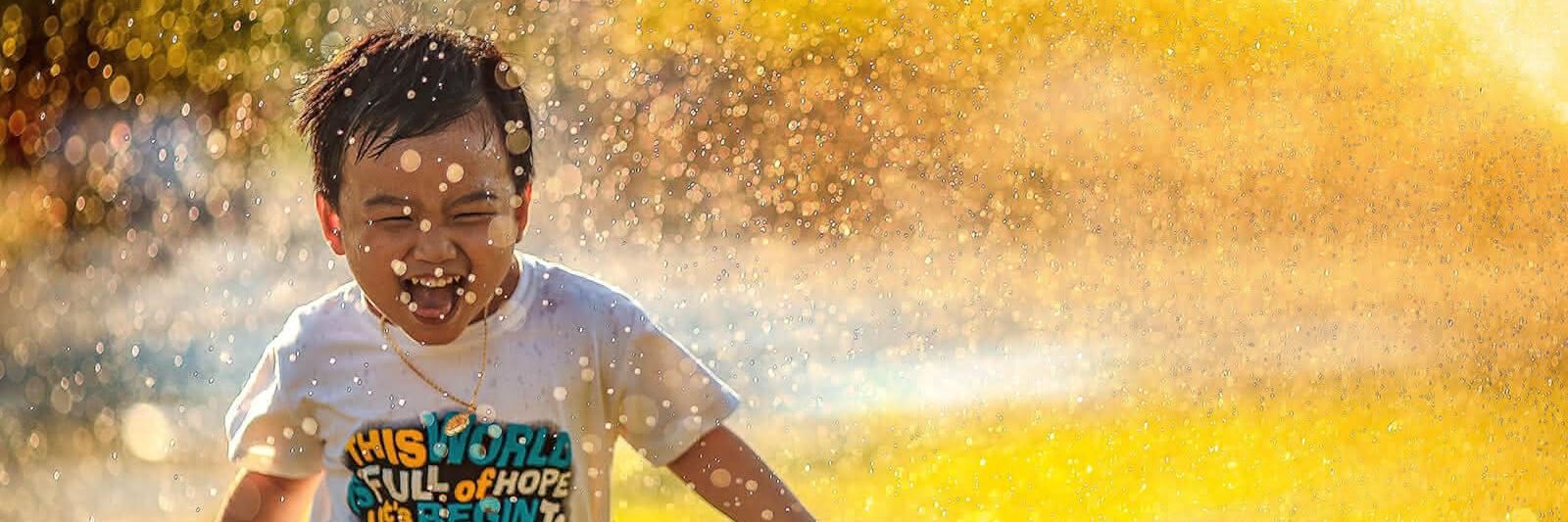 Kleiner Junge läuft durch das Wasser vom Rasensprenger